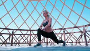 Woman performing leg lunges under a modern geometric canopy outdoors.