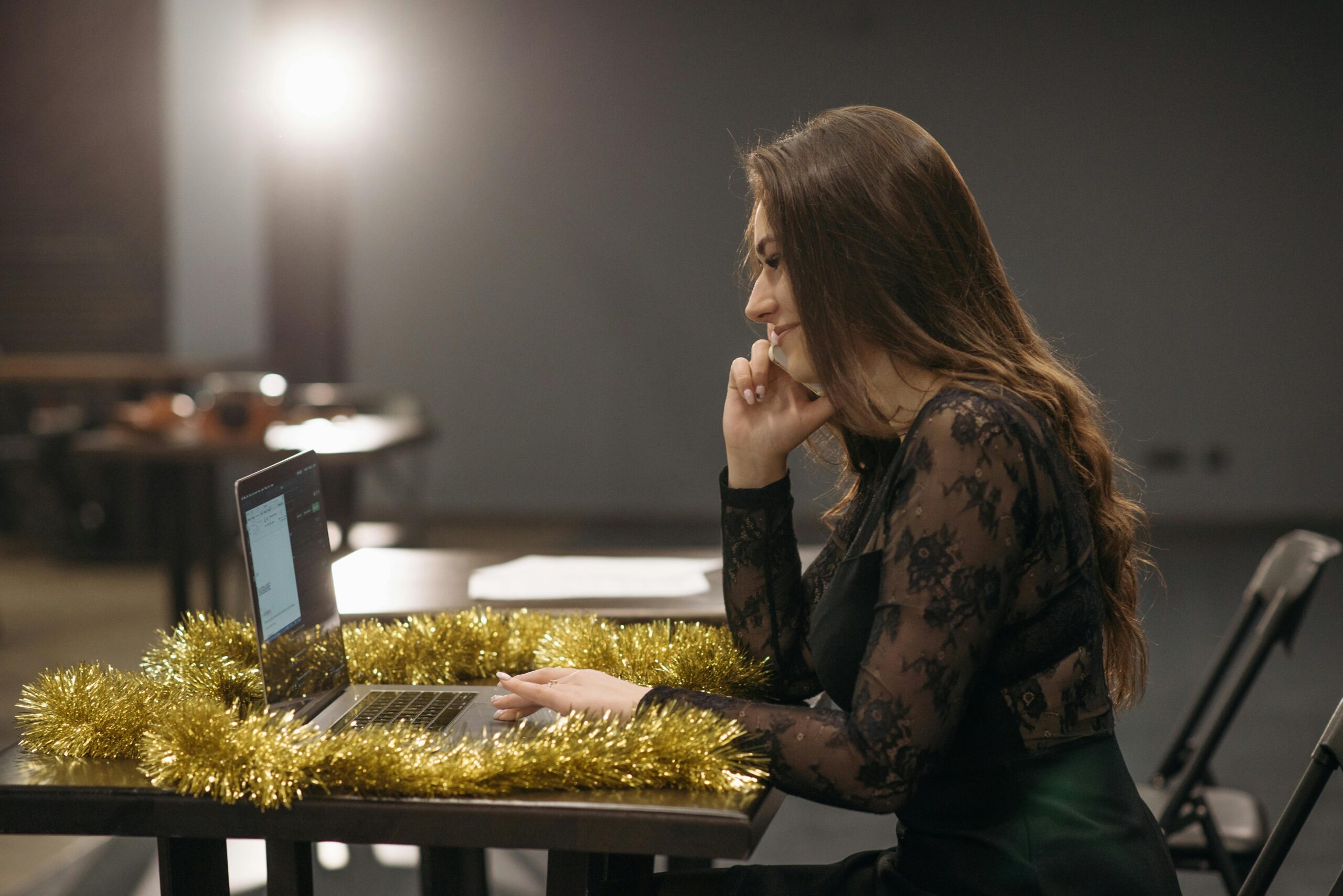Woman in elegant black dress working on a laptop at a festive decorated workspace. Perfect for holiday work themes.